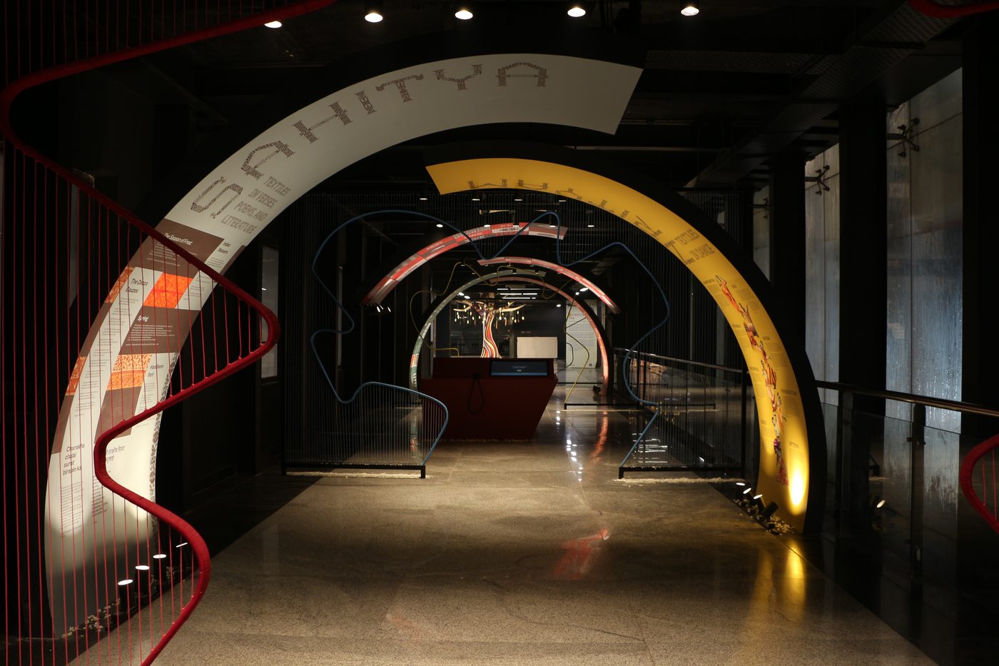 A darkened corridor at Handloom Haat, Janpath, lined with concentric painted arches in white, yellow and red, suspended thread sculptures visible at the far end.